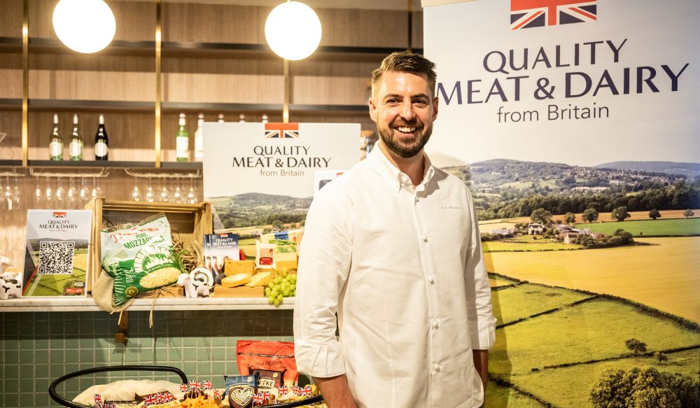 Man in chef whites stood in front of a quality meat and dairy from Britain banner